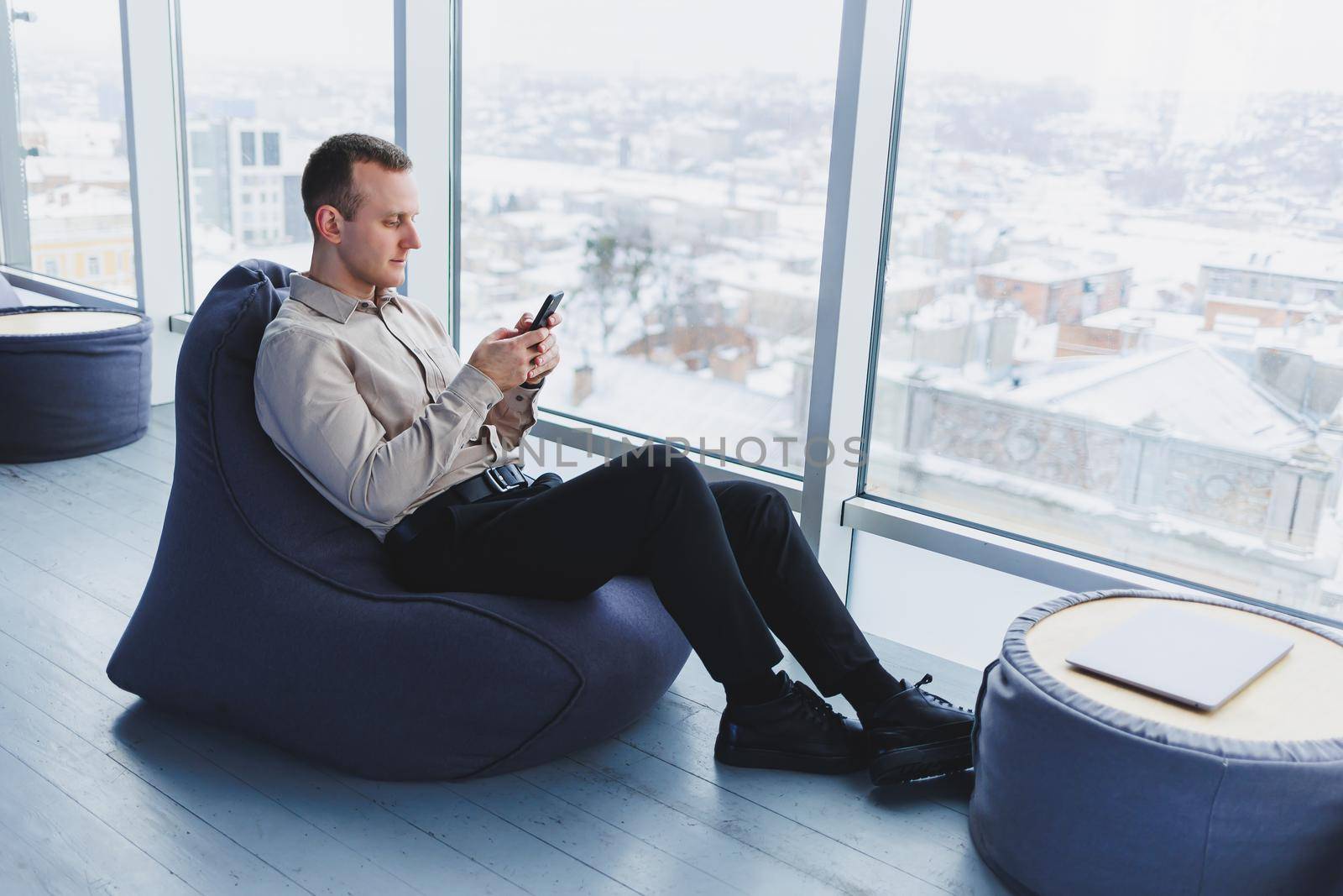 Successful male freelancer sitting in modern workspace and checking notifications on mobile phone in casual clothes. Remote work.