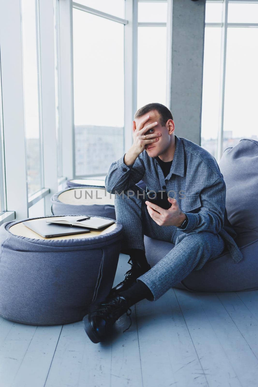 A handsome European young businessman in a coffee shop sits with a mobile phone and makes notes in a notebook. Wearing an elegant casual suit and sitting with a laptop in a public cafe
