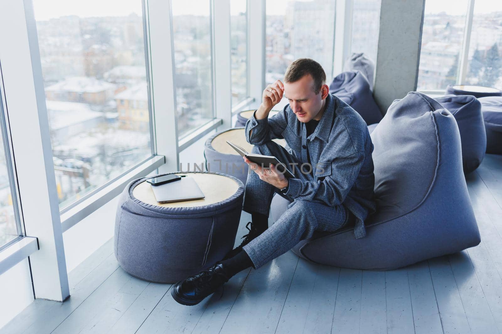 A male businessman in a casual suit resting in a comfortable pouf while working, an attractive freelancer in a suit works remotely and checks notes in a notebook