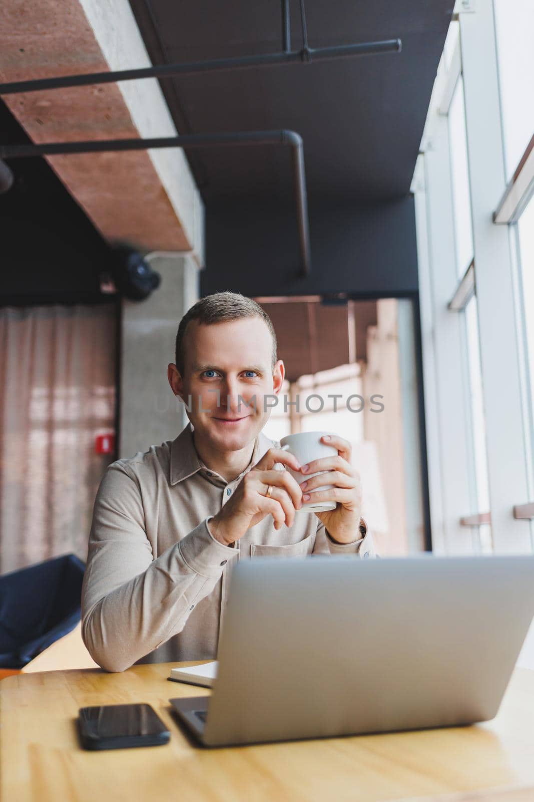 A young smart man is sitting in the office with a cup of coffee and is working on a project related to public cyber technology. Businessmen with laptop trying to meet deadlines in external marketing.