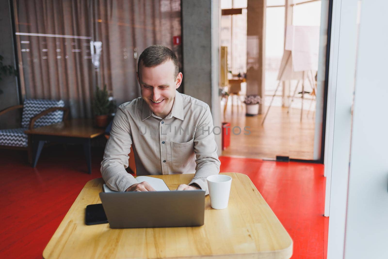 A young man sits at a table and opens a laptop computer while studying online. Modern digital computer works as a freelancer on a netbook in a cafe interior