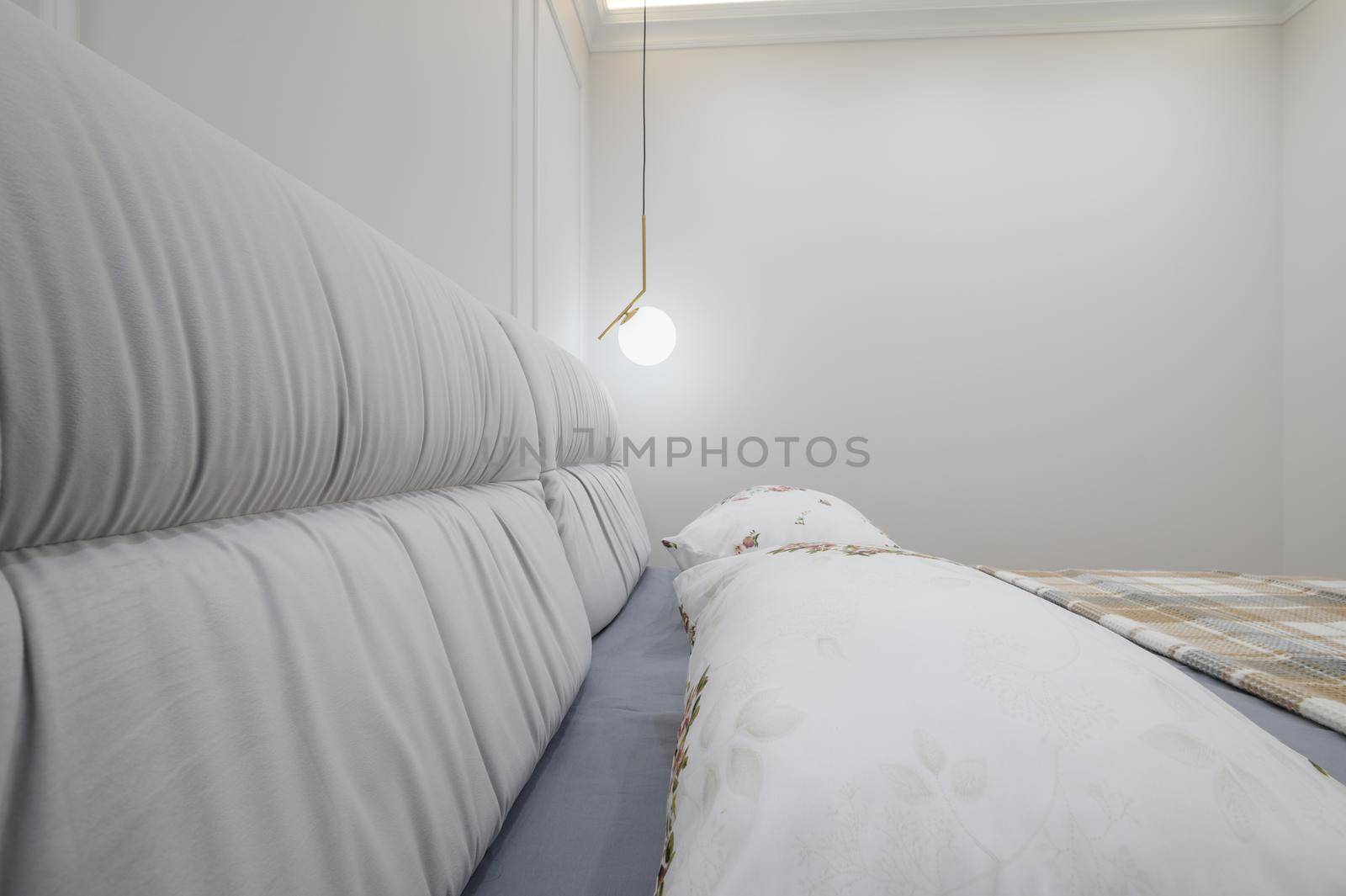Closeup to double bed with a plaid blanket and pillows on it in a cozy bedroom with white walls and a light fixtures