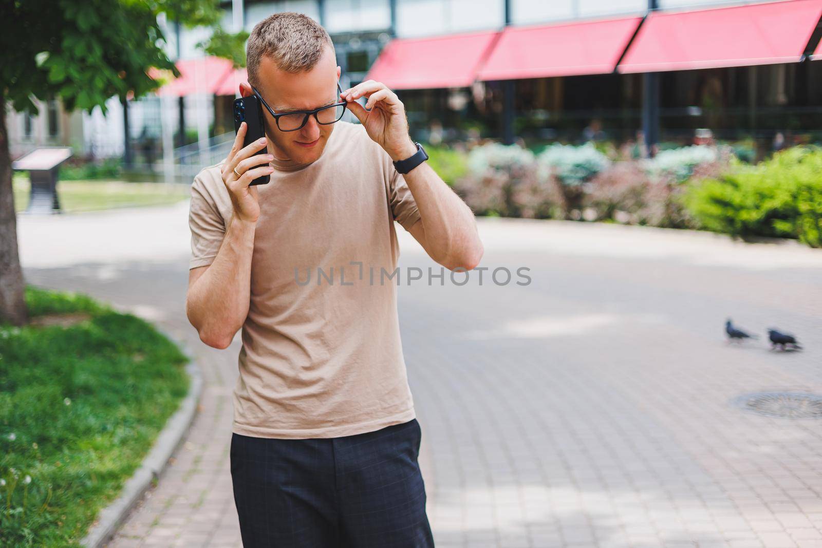 Portrait of handsome mature businessman holding messenger bag, wearing stylish eyeglasses looking at camera. Smiling middle aged man using smartphone, standing on the street. Mobile banking concept