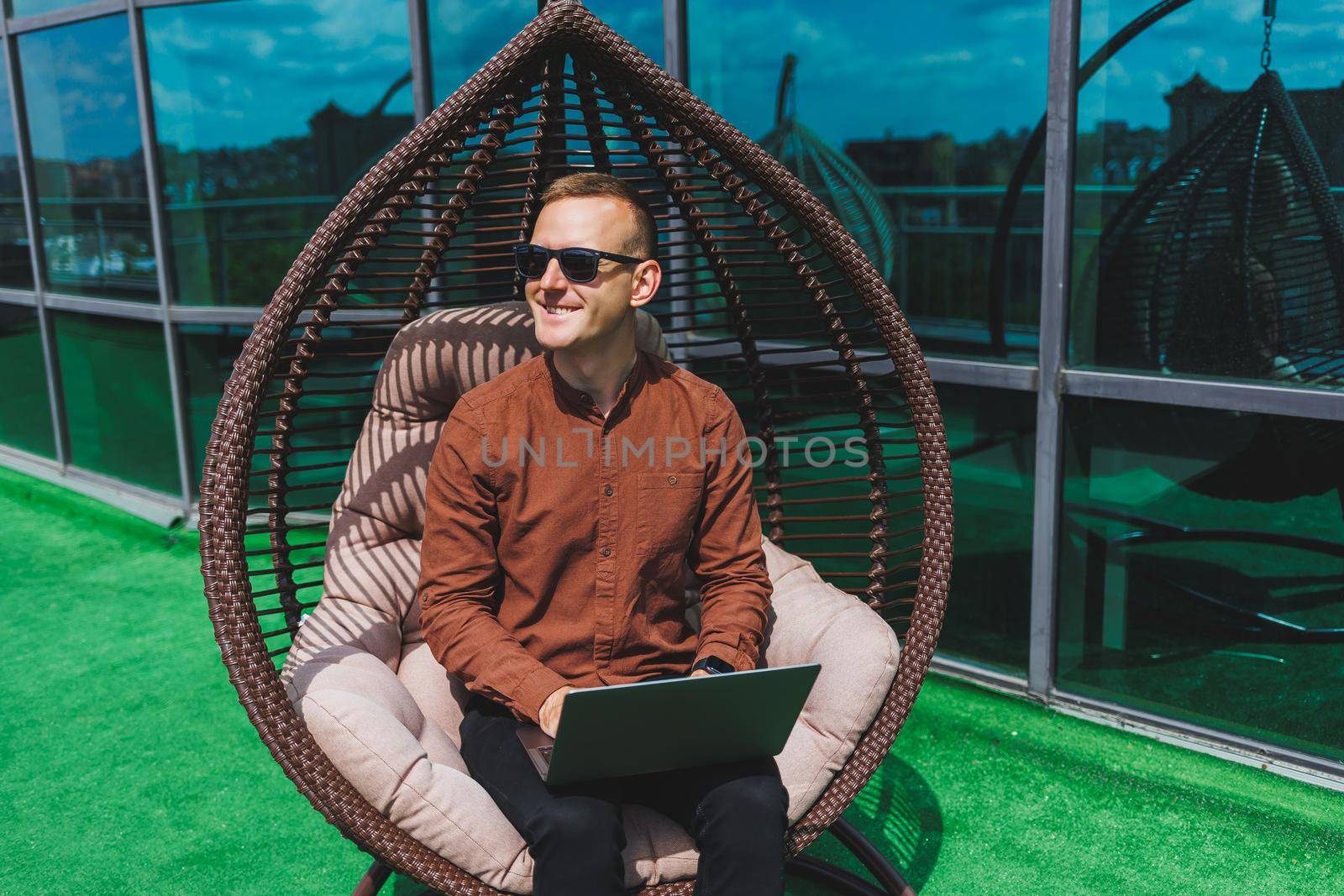 A businessman in formal wear sits on an armchair and looks at a laptop connected to a 4g wireless network on the terrace of a modern office while working remotely