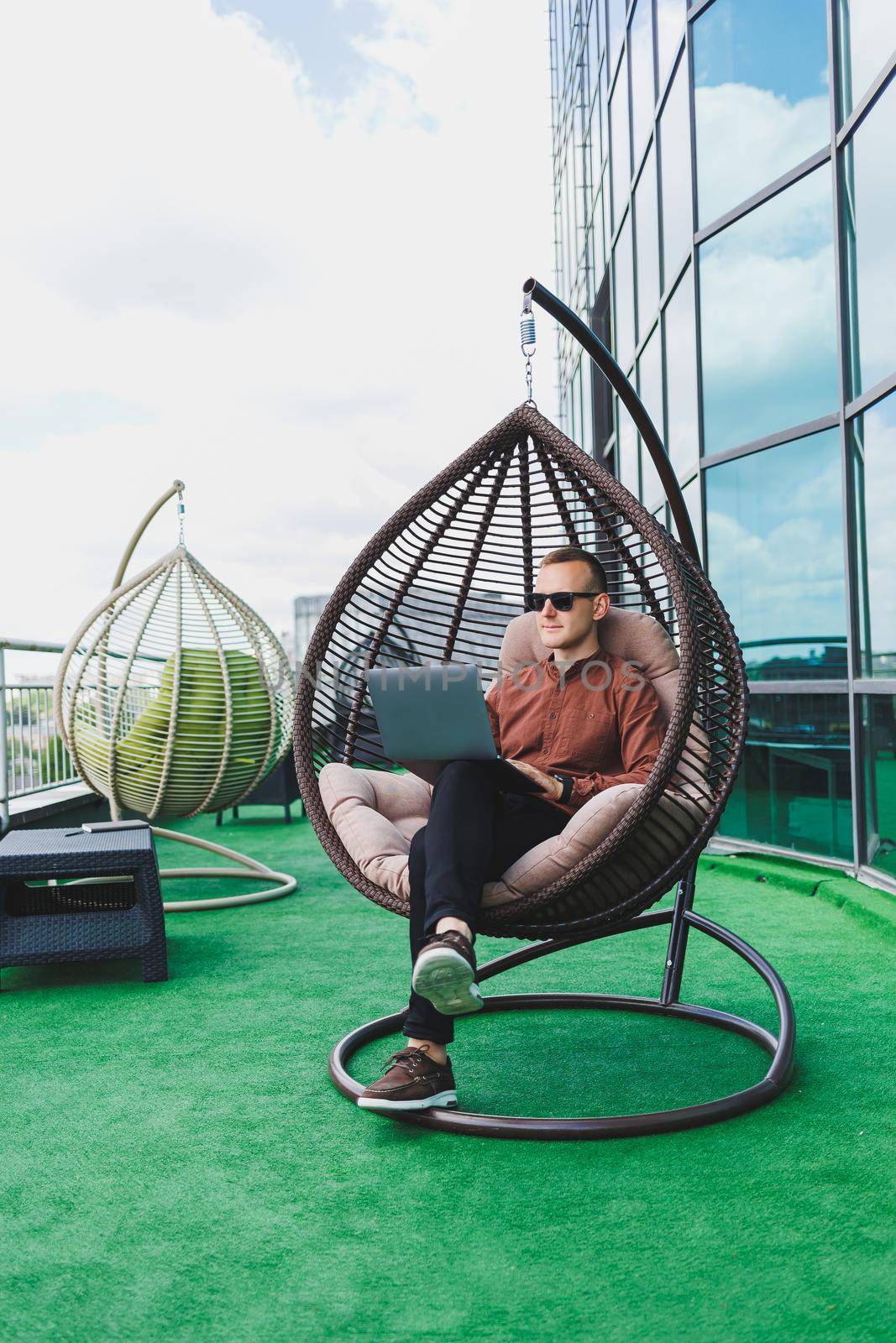 A businessman in formal wear sits on an armchair and looks at a laptop connected to a 4g wireless network on the terrace of a modern office while working remotely