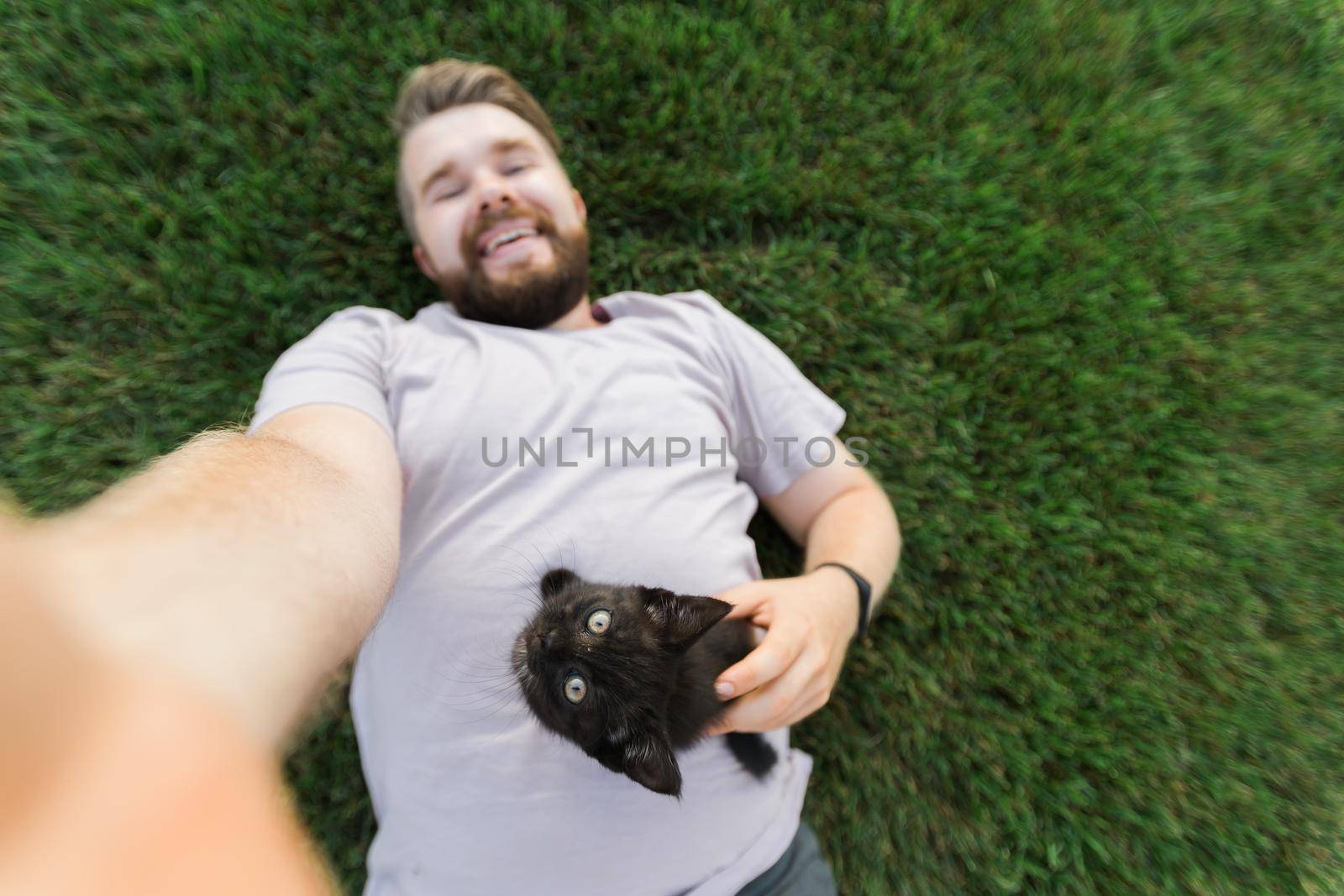 Man with little kitten lying and playing on grass - friendship love animals and pet owner