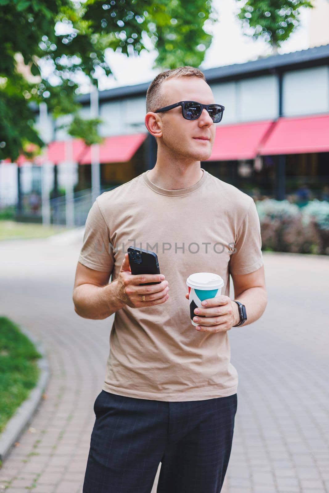 A bearded, smiling, stylish man in white shirt and sunglasses standing on the streets of the city and calling on mobile phone.