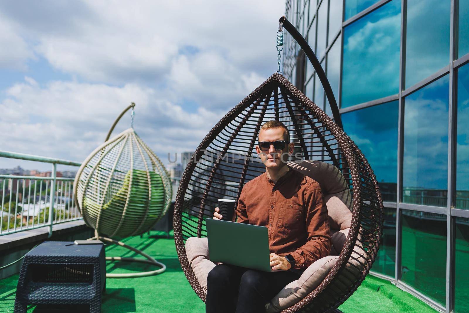 A businessman in formal wear sits on an armchair and looks at a laptop connected to a 4g wireless network on the terrace of a modern office while working remotely