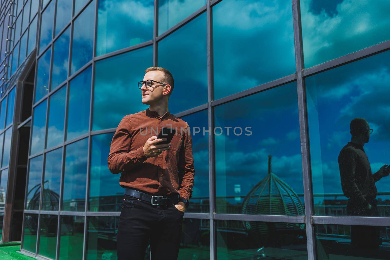 Happy man in classic glasses for vision correction with talking on terrace on mobile phone, smiling blogger browsing social media website