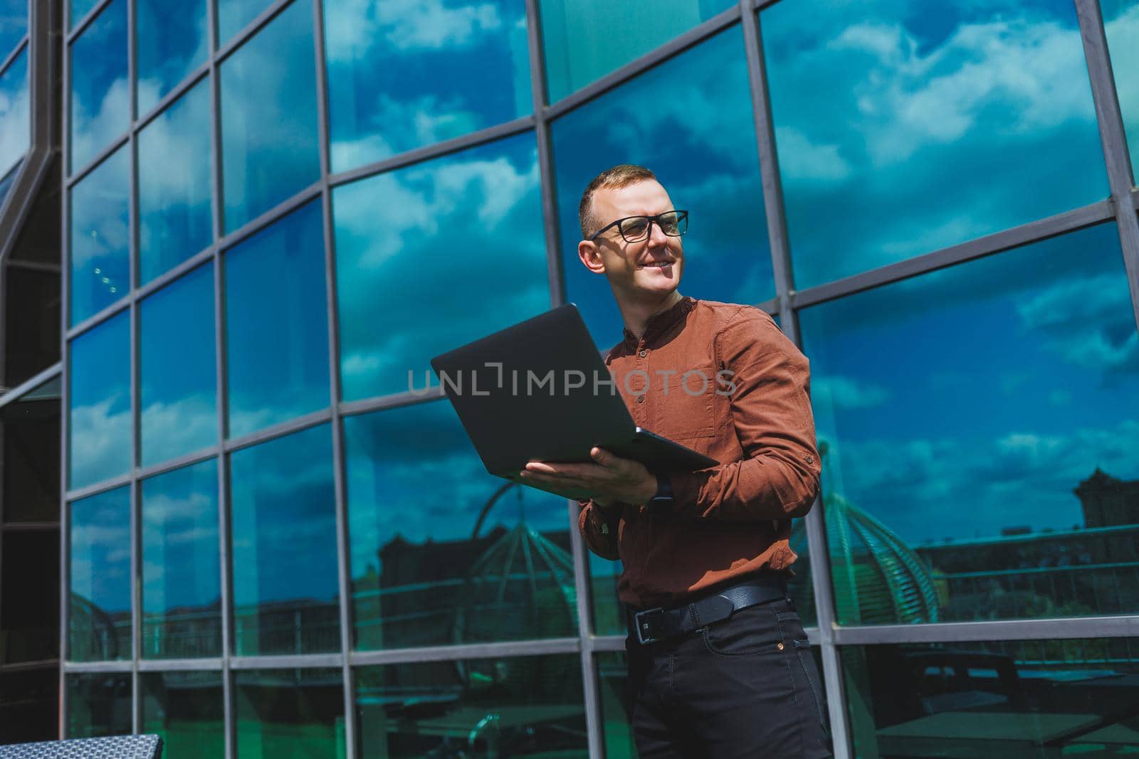 Cheerful businessman, formally dressed, pleased with received good news about contract details, sitting on office terrace with laptop, successful male entrepreneur