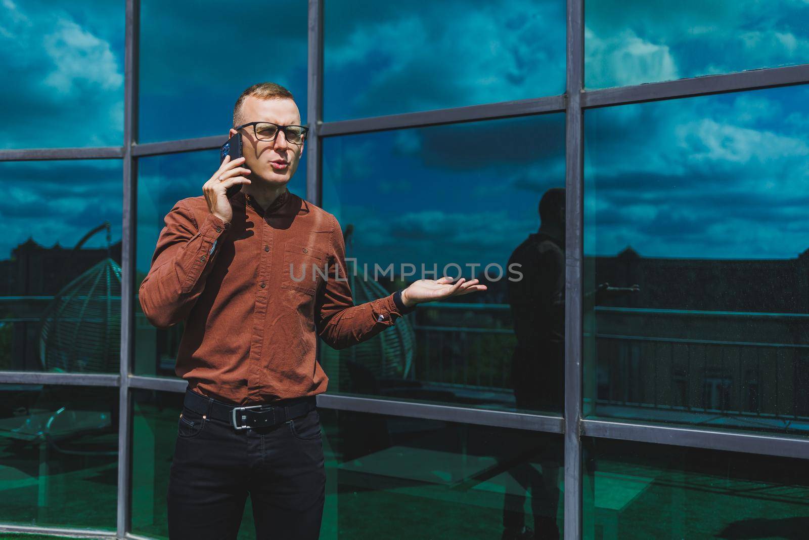 Happy man in classic glasses for vision correction with talking on terrace on mobile phone, smiling blogger browsing social media website