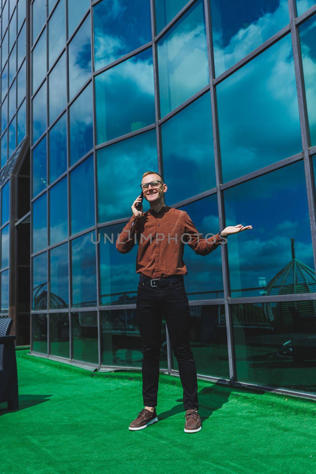 Happy man in classic glasses for vision correction with talking on terrace on mobile phone, smiling blogger browsing social media website