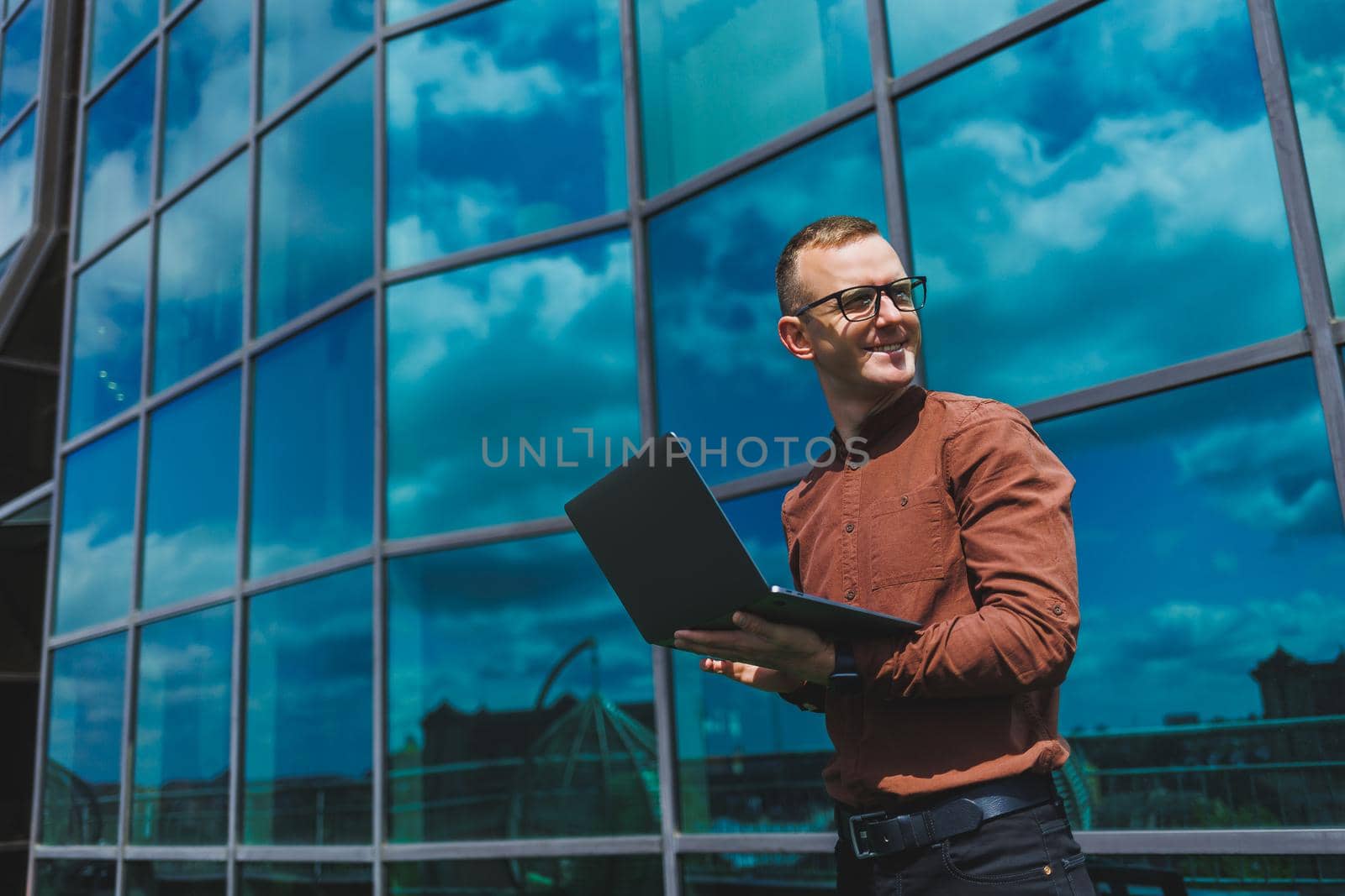 Cheerful businessman, formally dressed, pleased with received good news about contract details, sitting on office terrace with laptop, successful male entrepreneur
