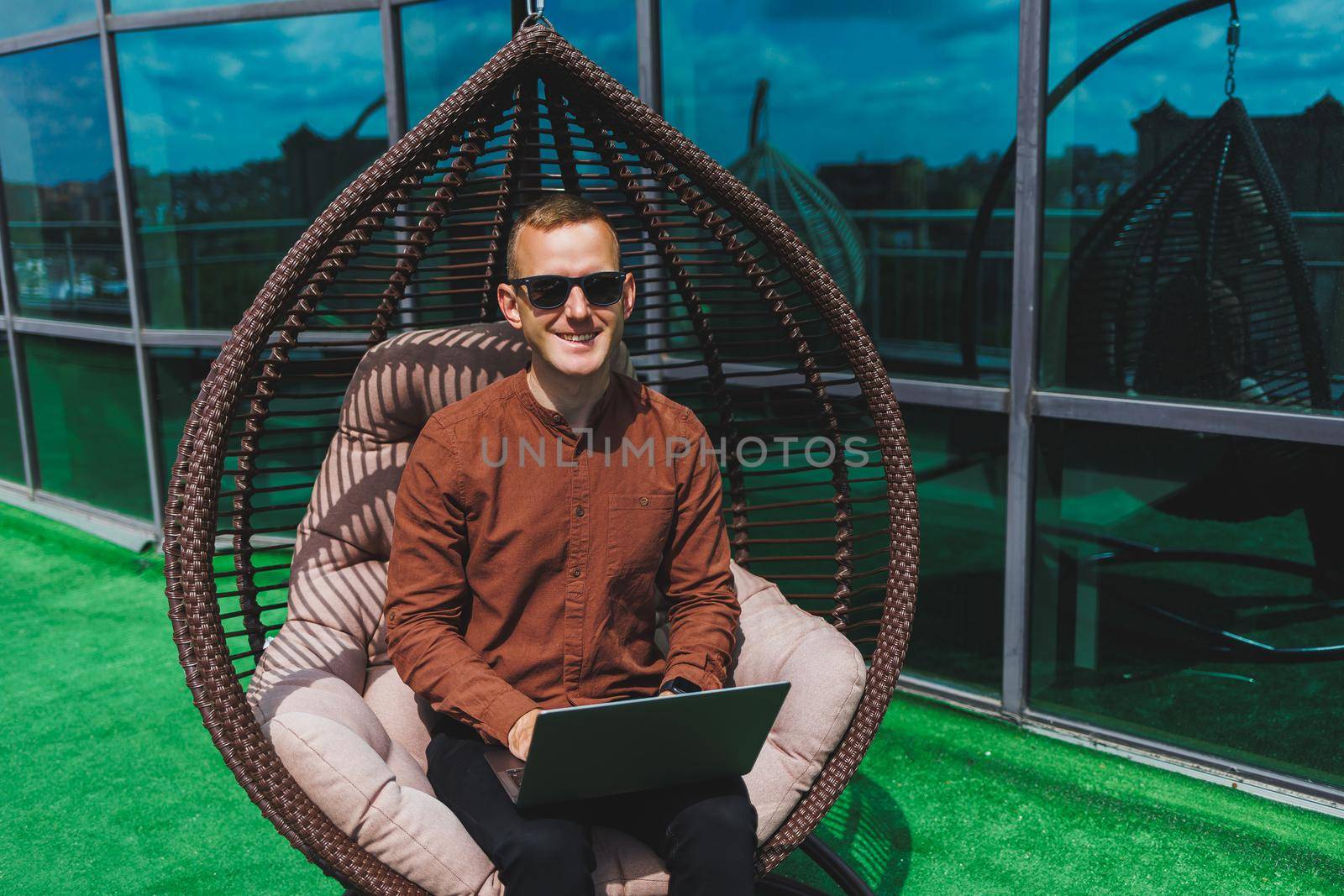 A businessman in formal wear sits on an armchair and looks at a laptop connected to a 4g wireless network on the terrace of a modern office while working remotely
