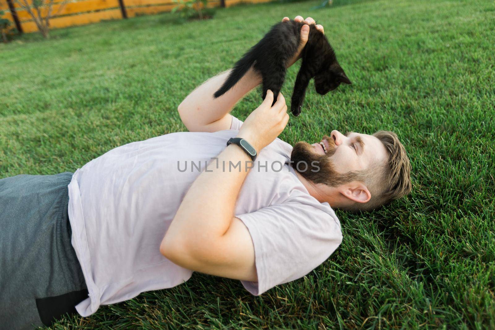 Man with little kitten lying and playing on grass - friendship love animals and pet owner