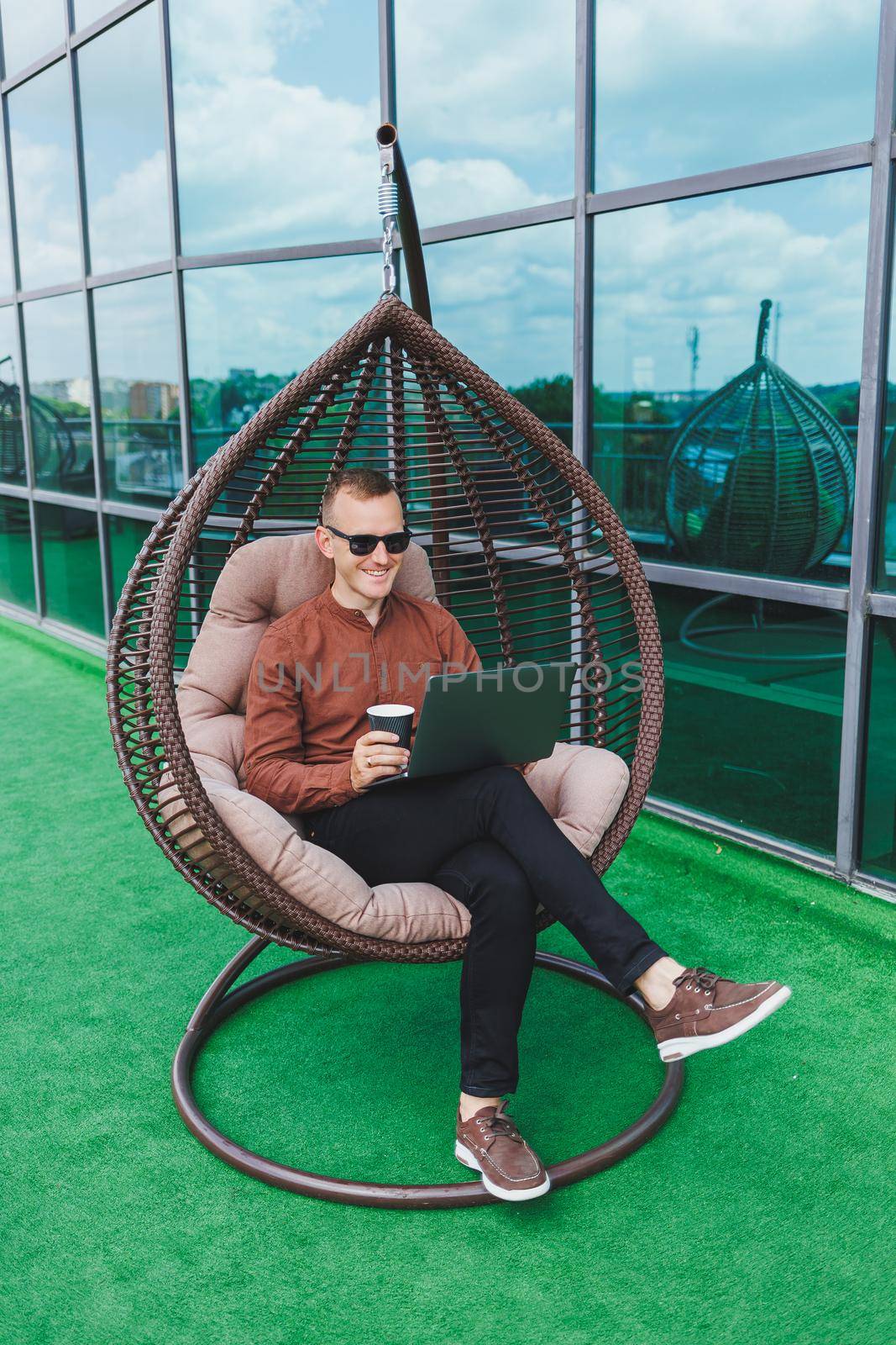 A businessman in formal wear sits on an armchair and looks at a laptop connected to a 4g wireless network on the terrace of a modern office while working remotely
