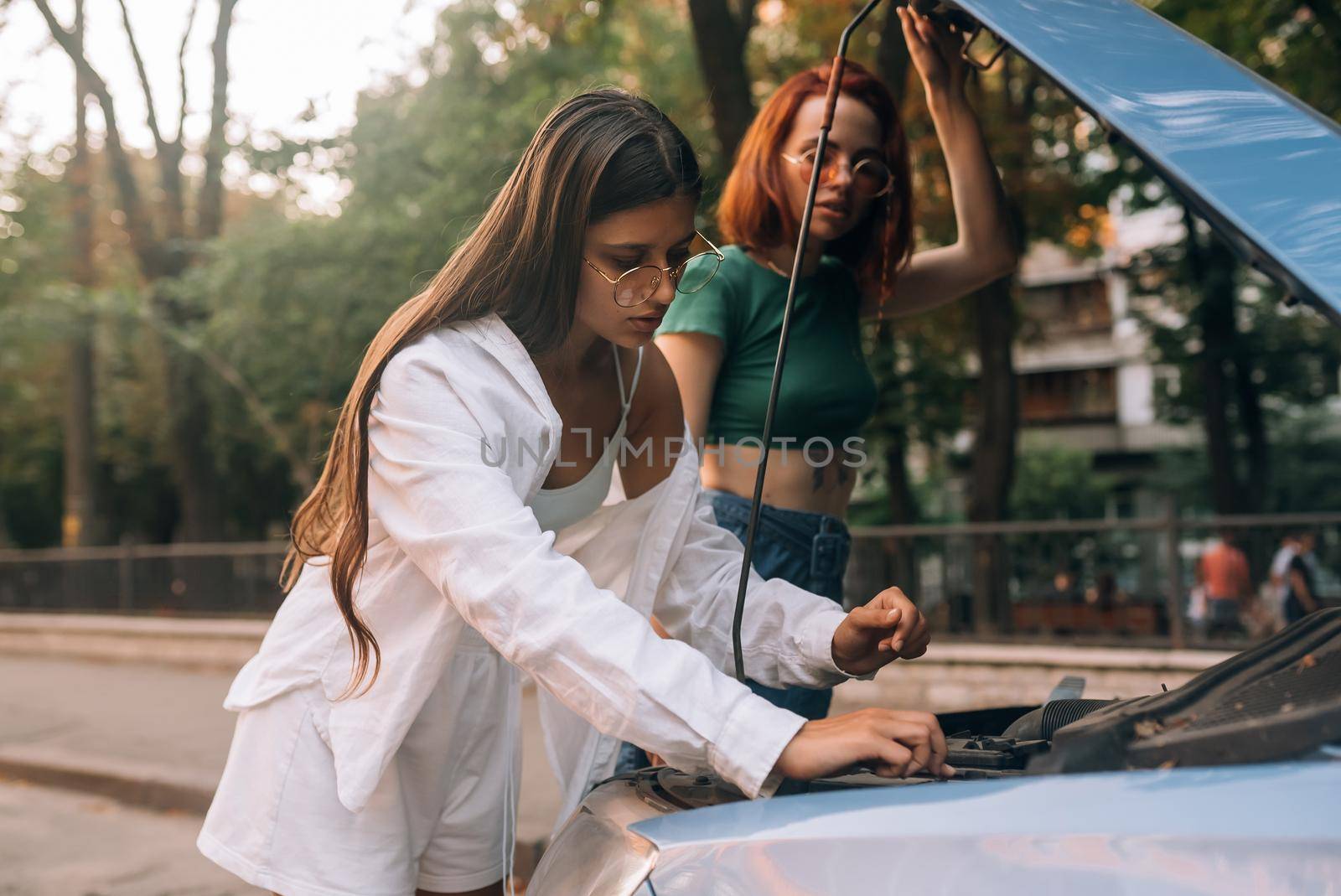 Two women with broken car on the road. Open hood by teksomolika