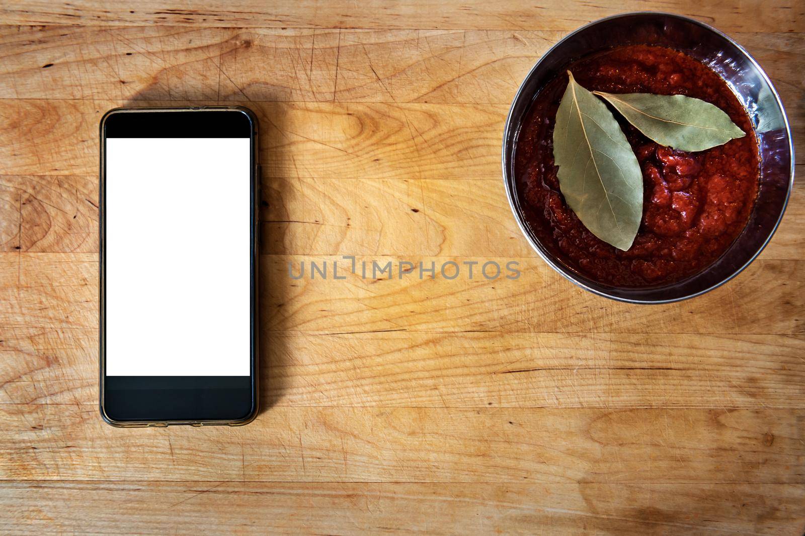 old wooden board with tomato sauce and laurel leaves in a bowl, with a smart-phone. Flat lay, top view with copy space