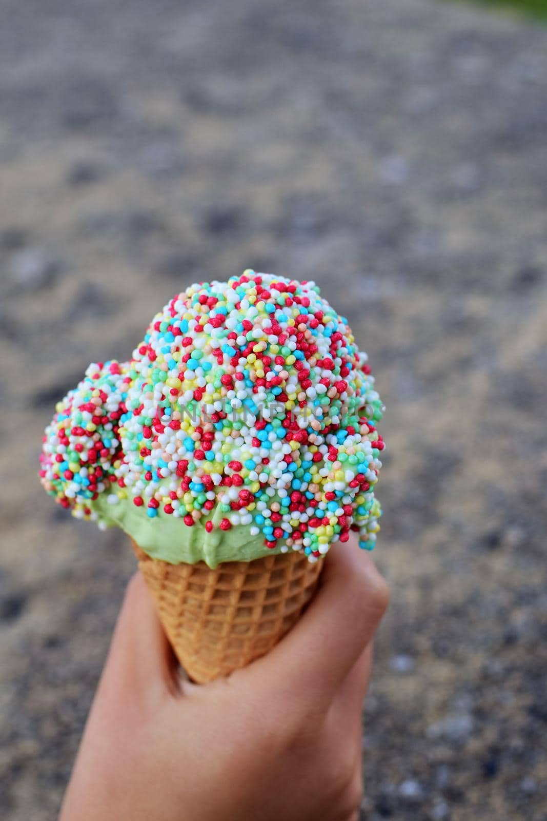 Ice cream with colorful sugar sprinkles in hand as a close-up against a grey blurred background