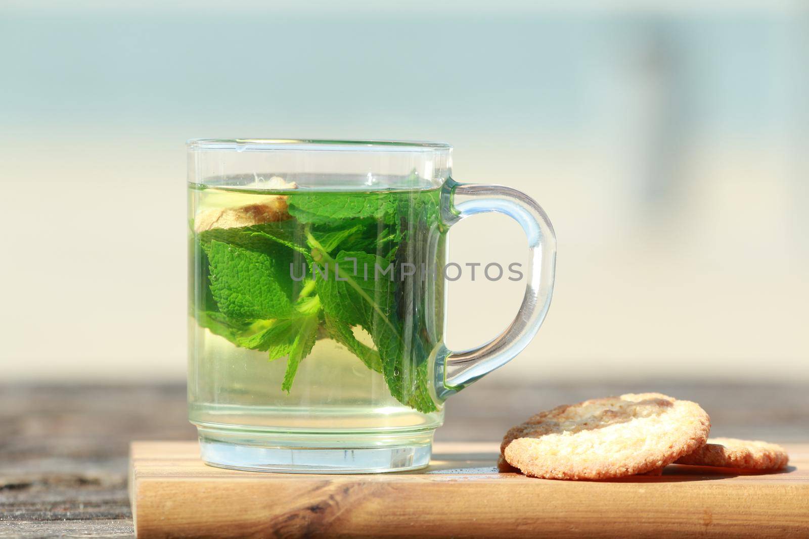 Peppermint tea with green leaves and cookies in front of a beach by Luise123