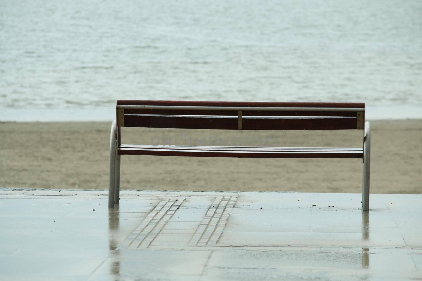 Wooden bench in front of the beach and the ocean on a rainy day by Luise123