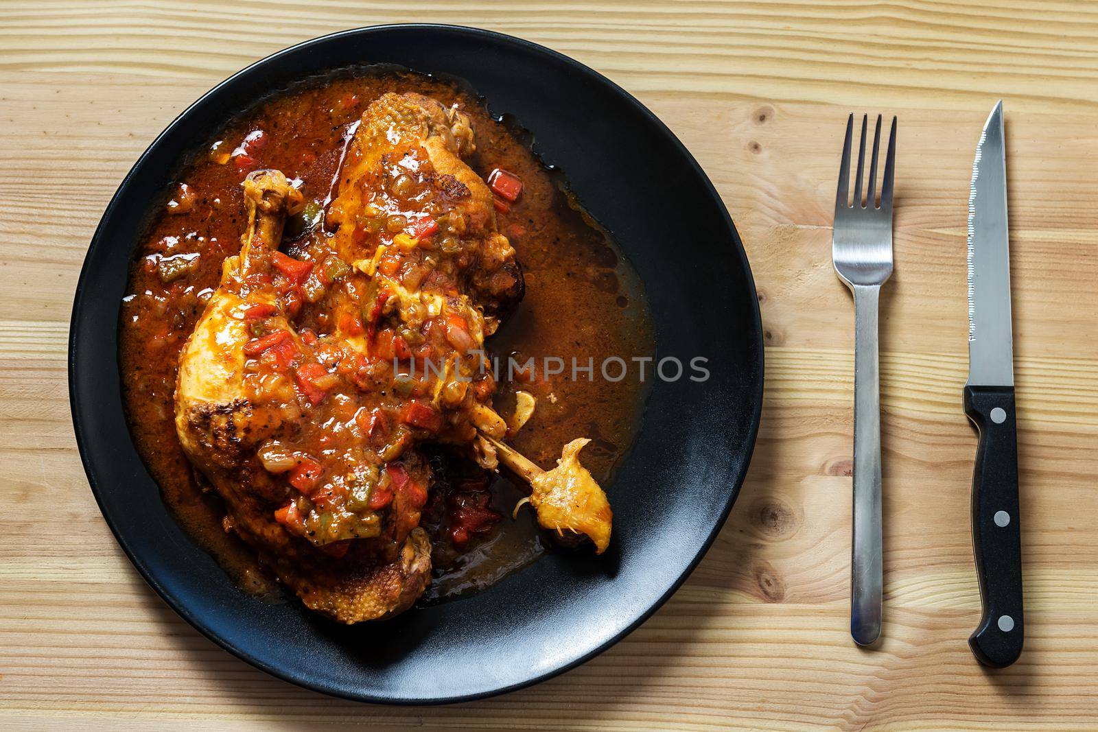 top view of a traditional dish of chicken with vegetables in sauce. On the wooden table there are cutlery. Flat lay