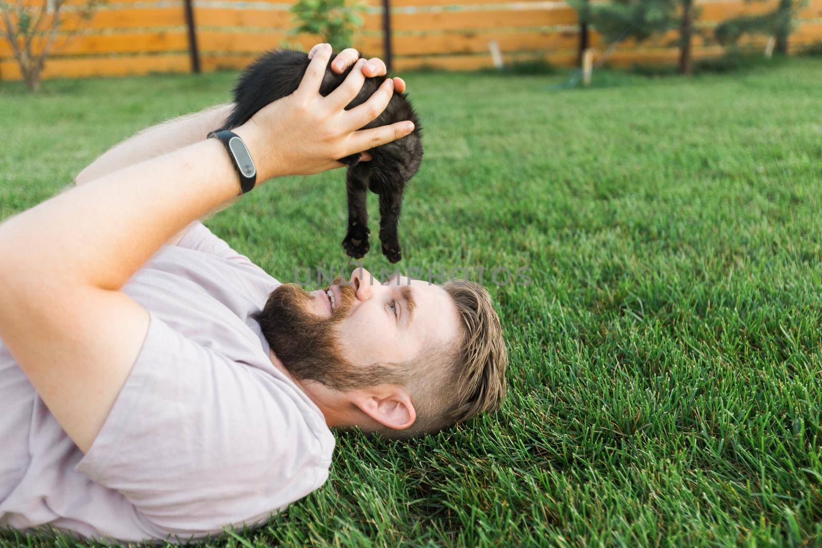 Man with little kitten lying and playing on grass - friendship love animals and pet owner