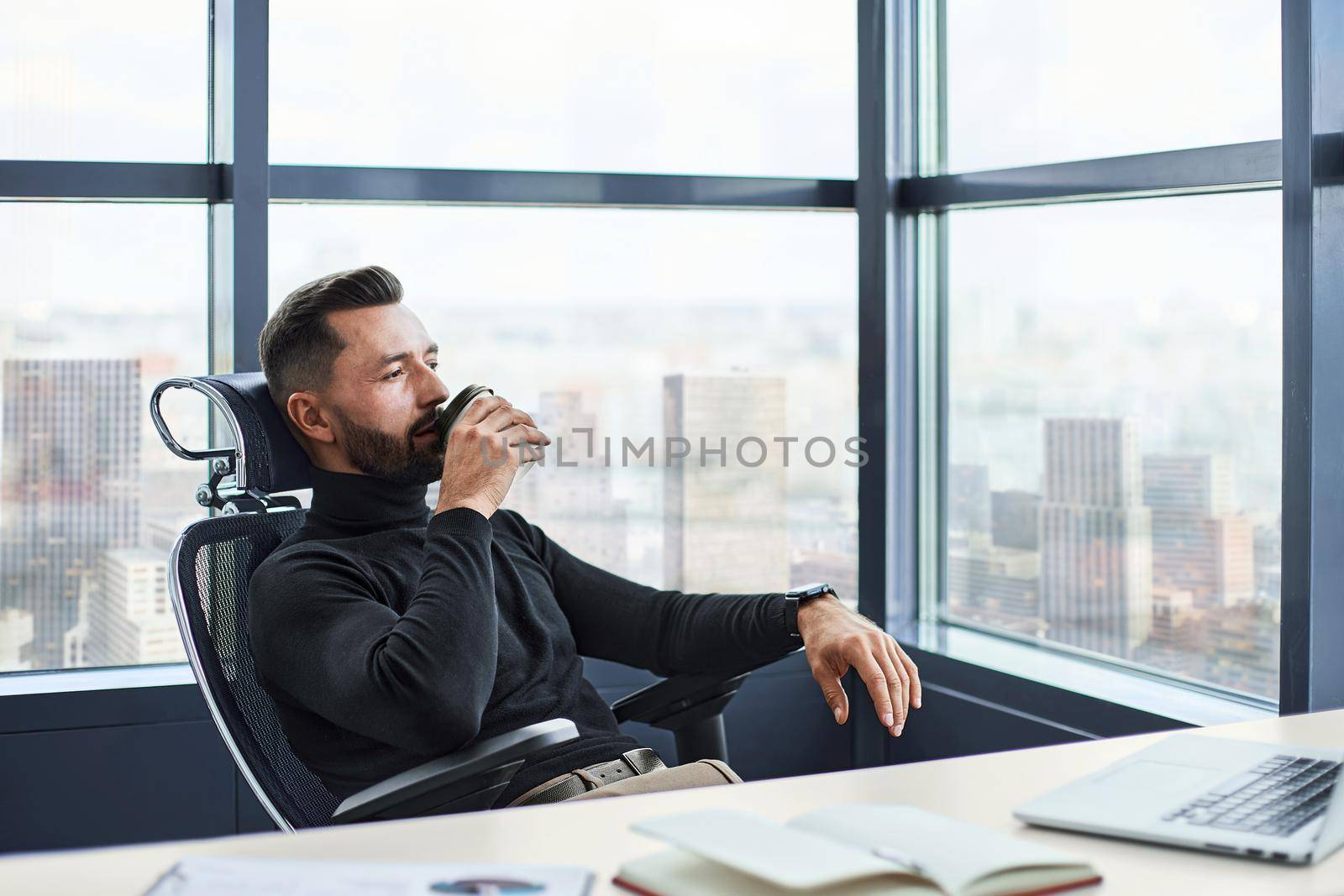 tired businessman drinks coffee sitting at his desk. close-up.