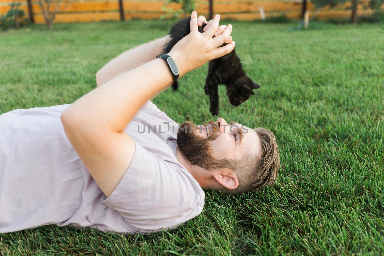 Man with little kitten lying and playing on grass - friendship love animals and pet owner