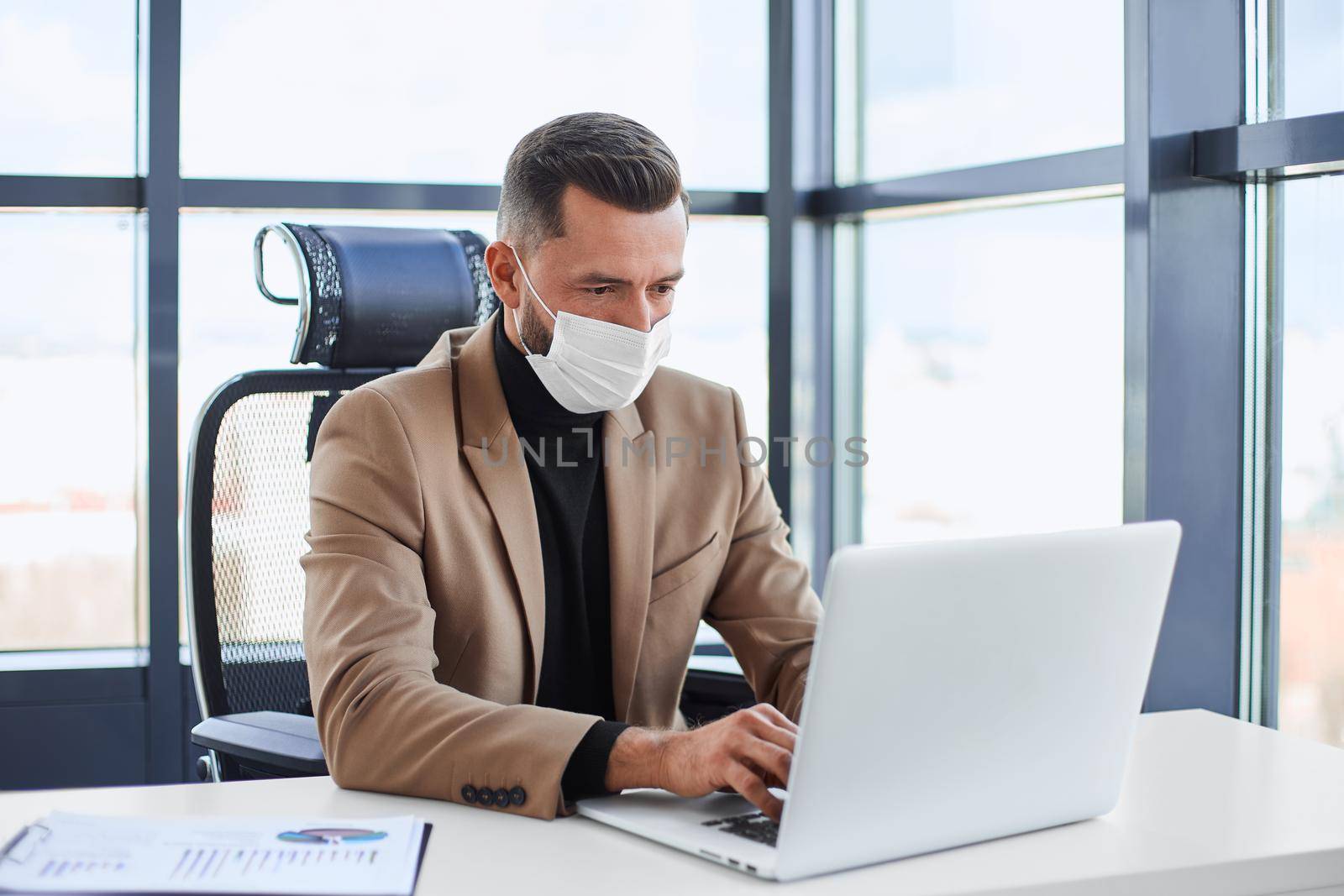 businessman in a protective mask working on a laptop. by SmartPhotoLab