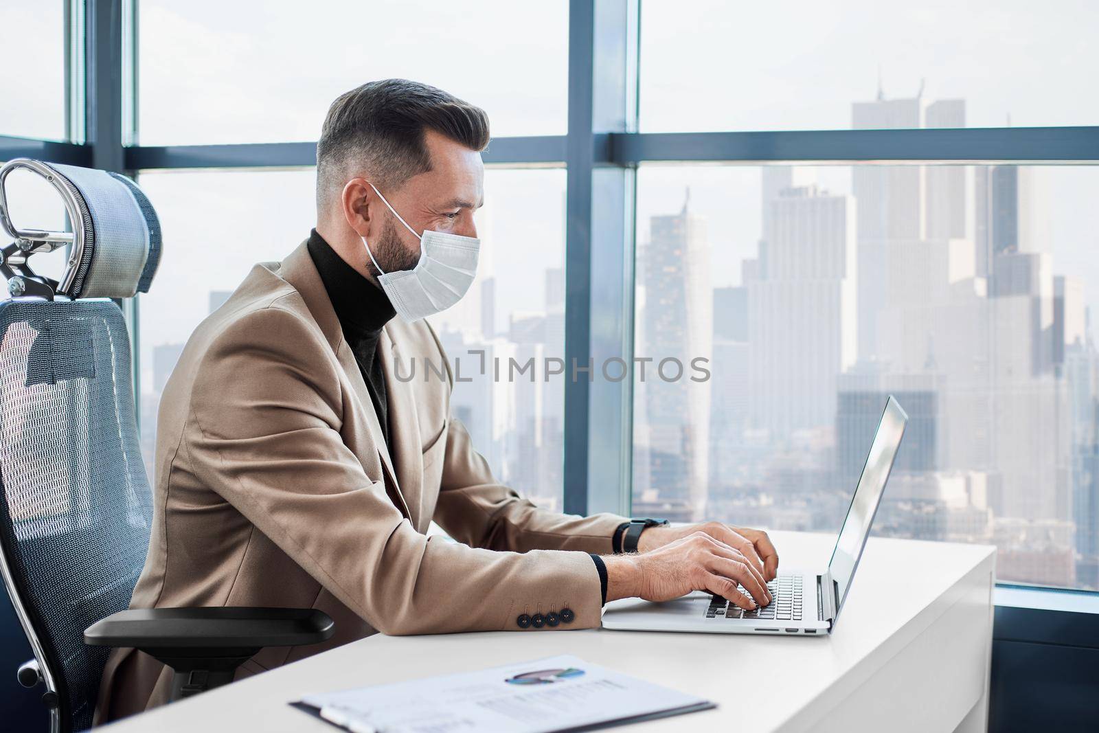 businessman in a protective mask working on a laptop in the office. by SmartPhotoLab