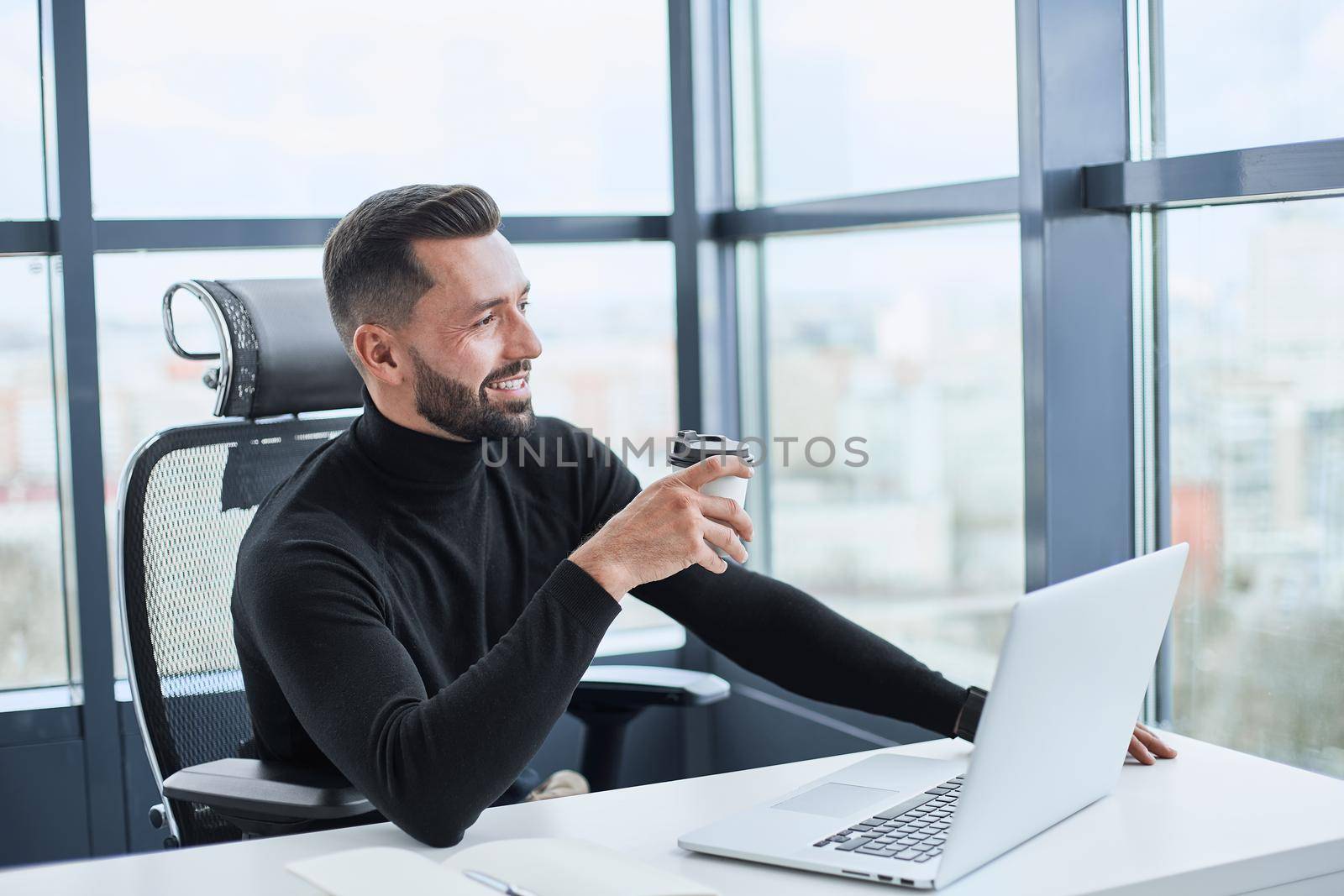 tired businessman drinks coffee sitting at his desk. by SmartPhotoLab