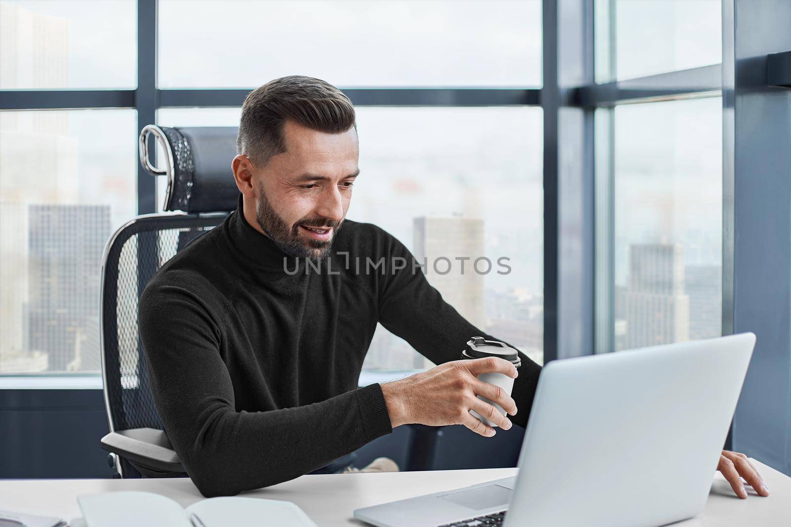 tired businessman drinks coffee sitting at his desk. close-up.