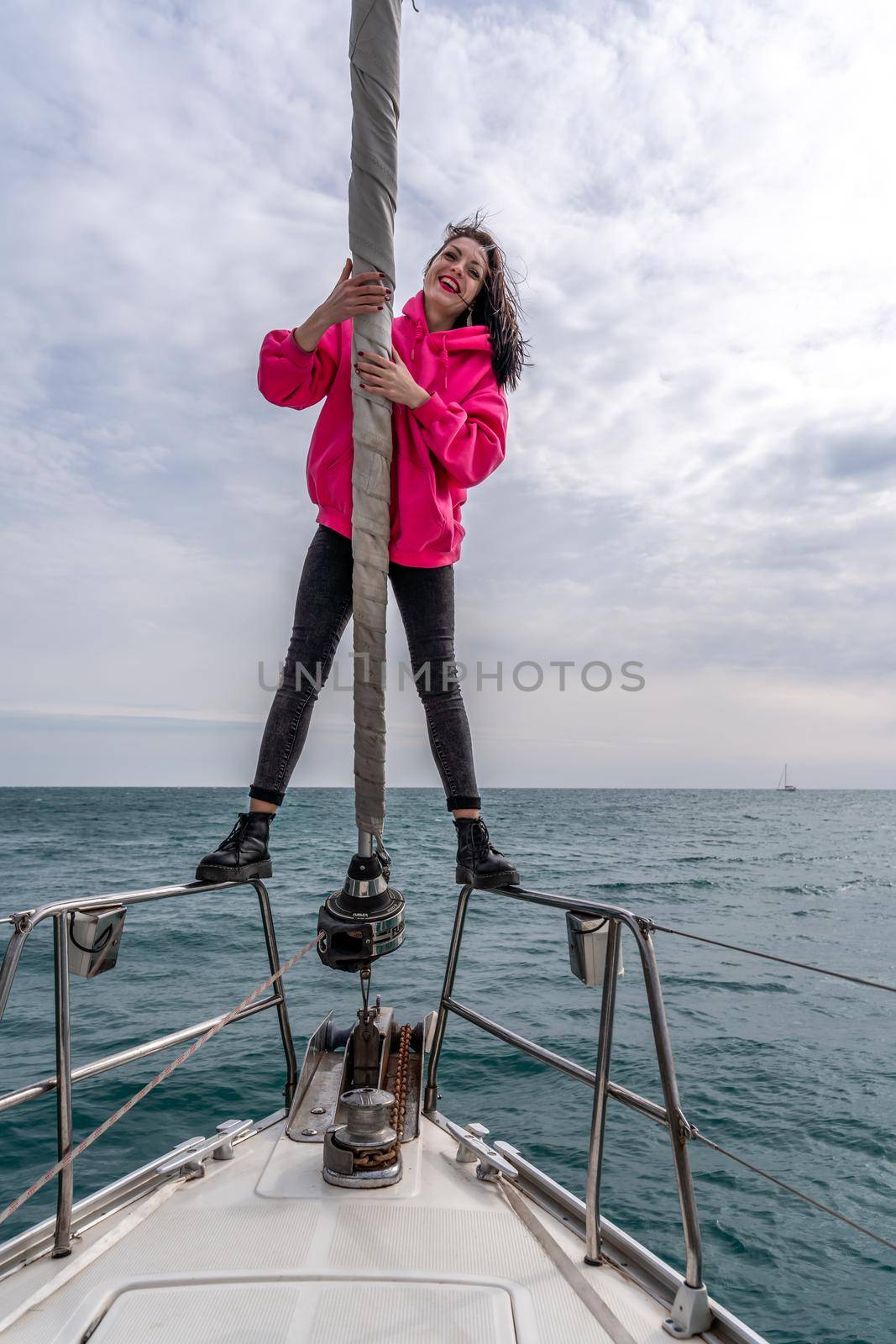 Woman standing on the nose of the yacht at a sunny summer day, breeze developing hair, beautiful sea on background.