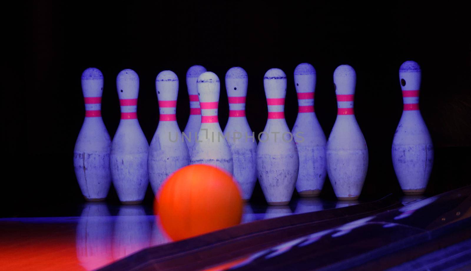 Orange bowling ball rolls to the pins in a dark bowling environment