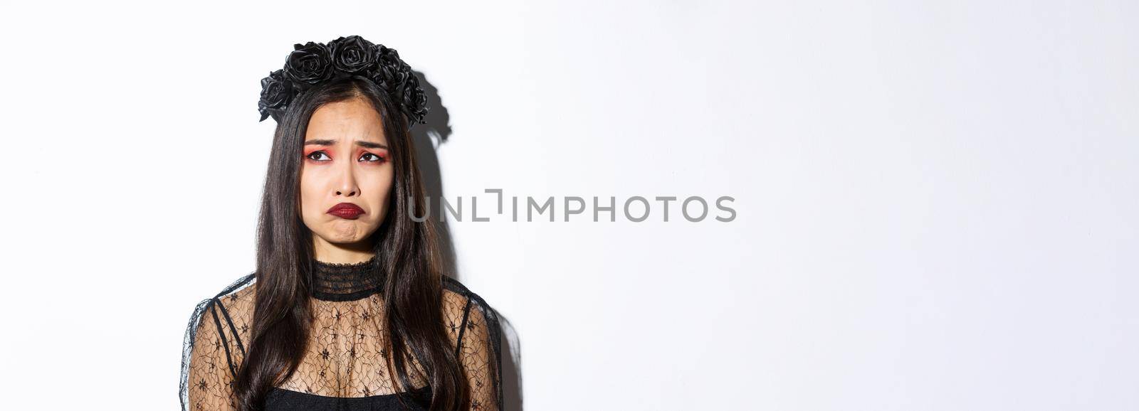 Close-up of sulking sad girl in witch costume looking at upper left corner disappointed, feeling miserable on halloween, standing over white background by Benzoix