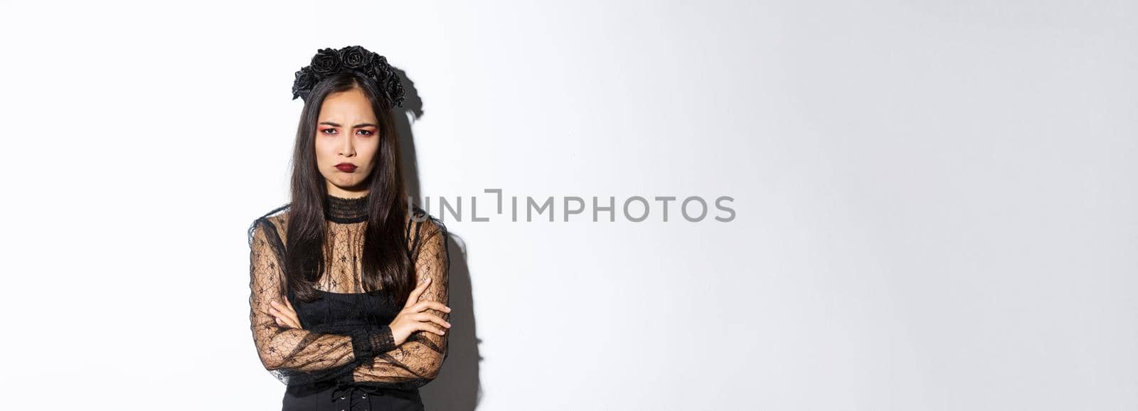 Image of angry and offended asian girl complaining on something, cross arms and sulking, looking insulted or jealous, standing over white background in halloween party dress by Benzoix