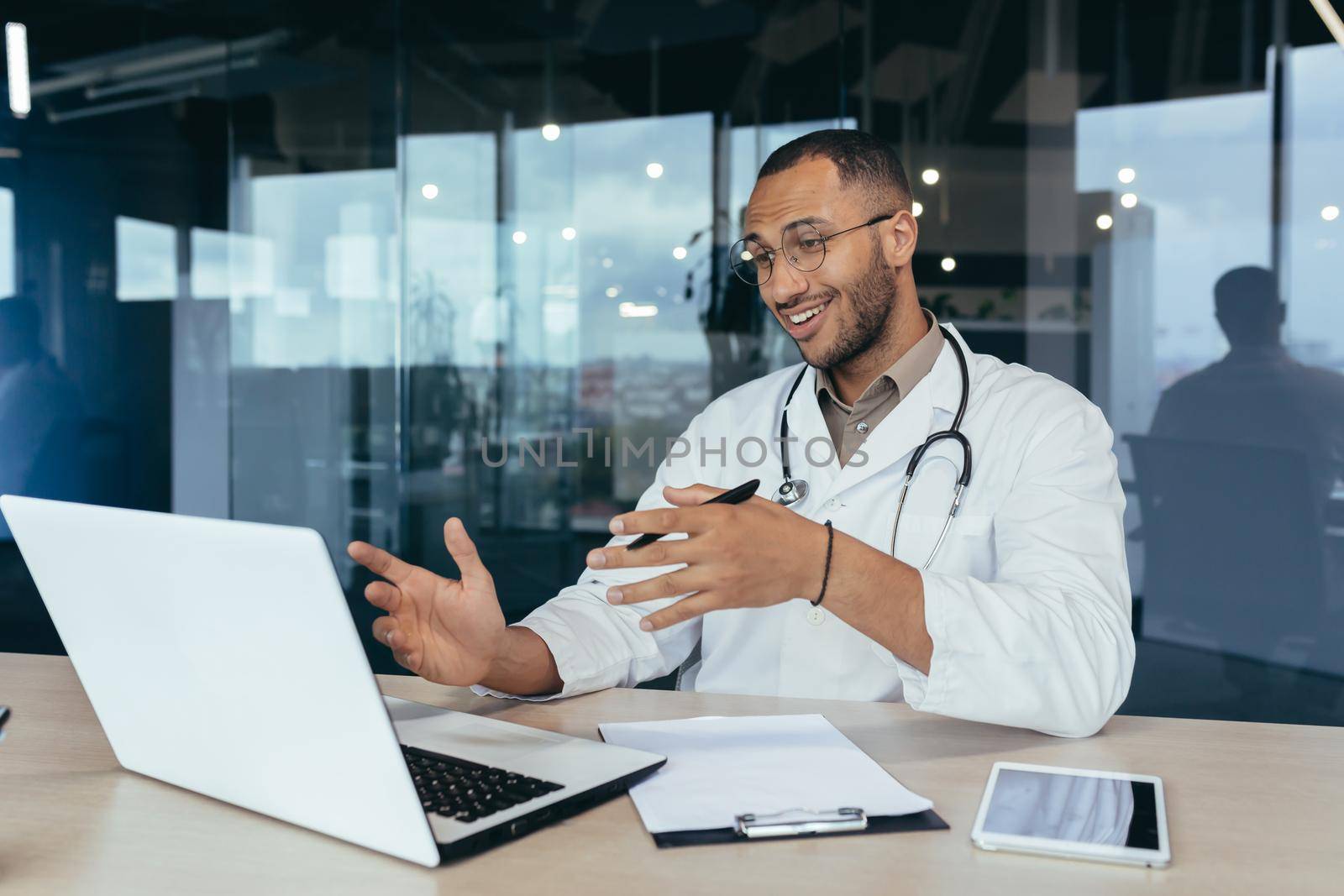 Cheerful african american doctor talking on video call, man using laptop for remote online consultation of patients, doctor working inside modern clinic in office.