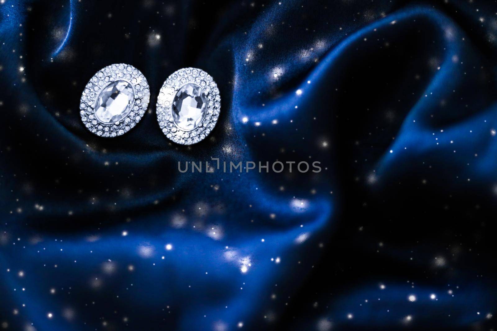 Jewellery brand, Christmas shopping and New Years gift concept - Luxury diamond earrings on dark blue silk with snow glitter, holiday winter magic jewelery present