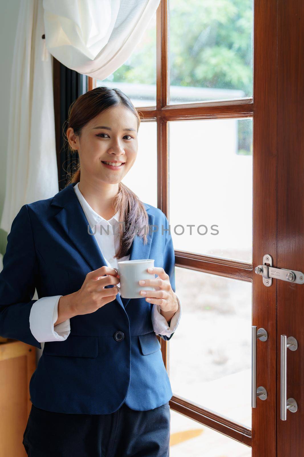 A portrait of an Asian businesswoman showing a happy smiling face holding a cup of coffee during a break.