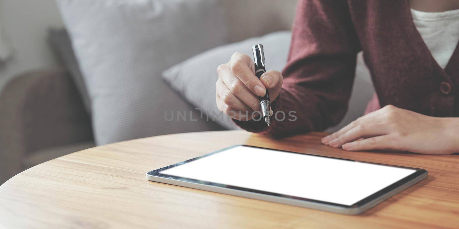 Closeup of a young woman using smart pen technology for working and writing on digital tablet screen by wichayada