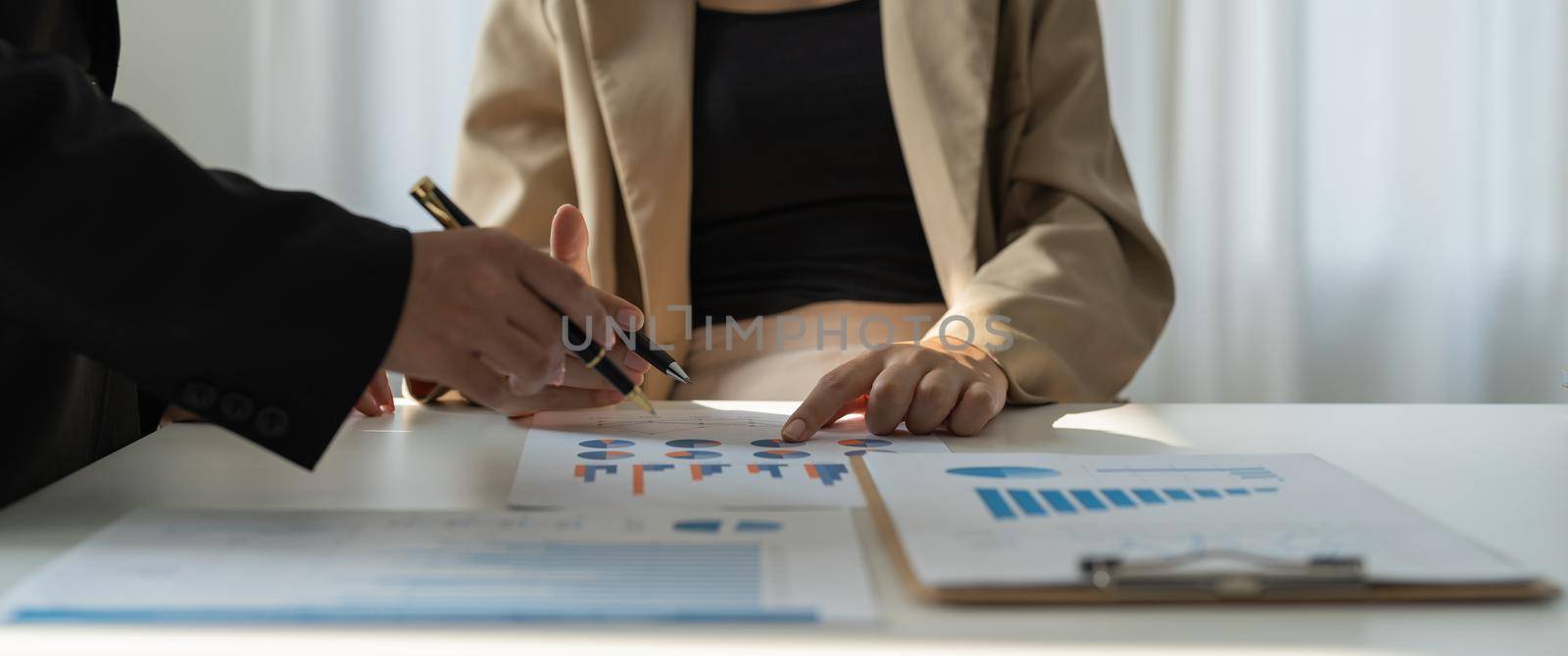 Two business people working together to analyze, work together to discuss company financial statistics, brainstorm ideas, and graph documents on the table.