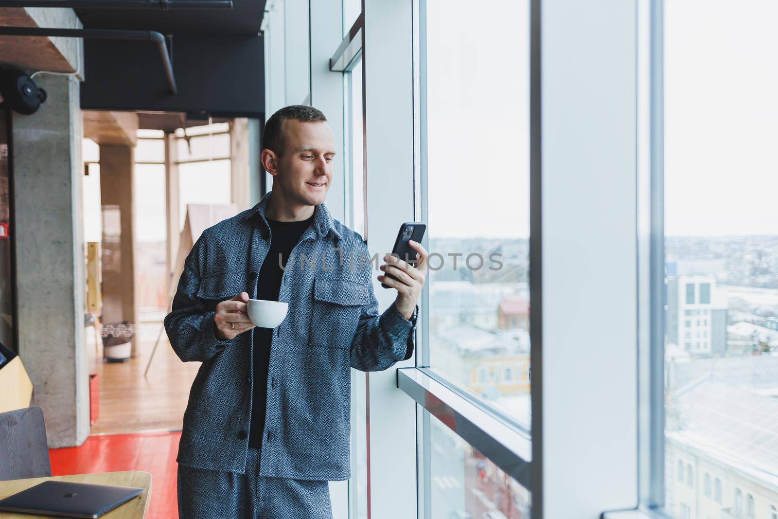 European male freelancer in checking notification on smartphone about money transactions, doing business online, working remotely while in cafe and drinking coffee