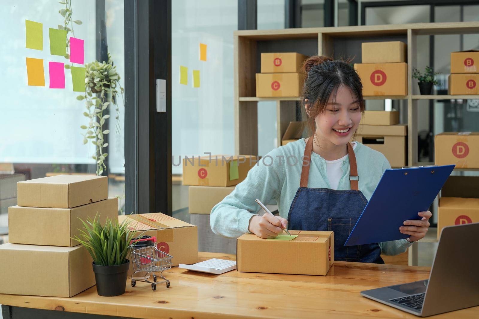 Asian business owner working, checking order to confirm before sending to customer. Female entrepreneur packaging box for delivery