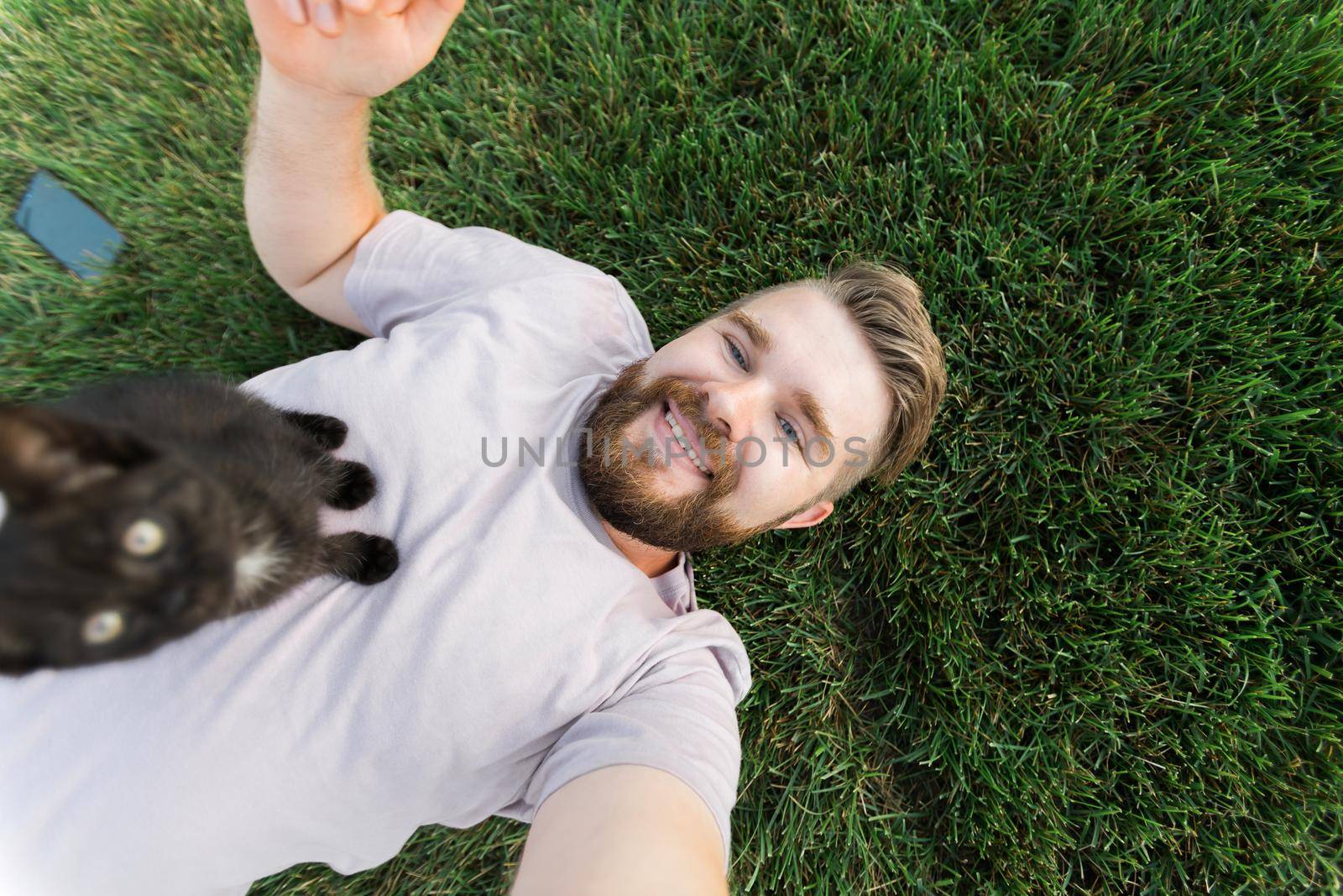 Man with little kitten lying and playing on grass - friendship love animals and pet owner concept by Satura86
