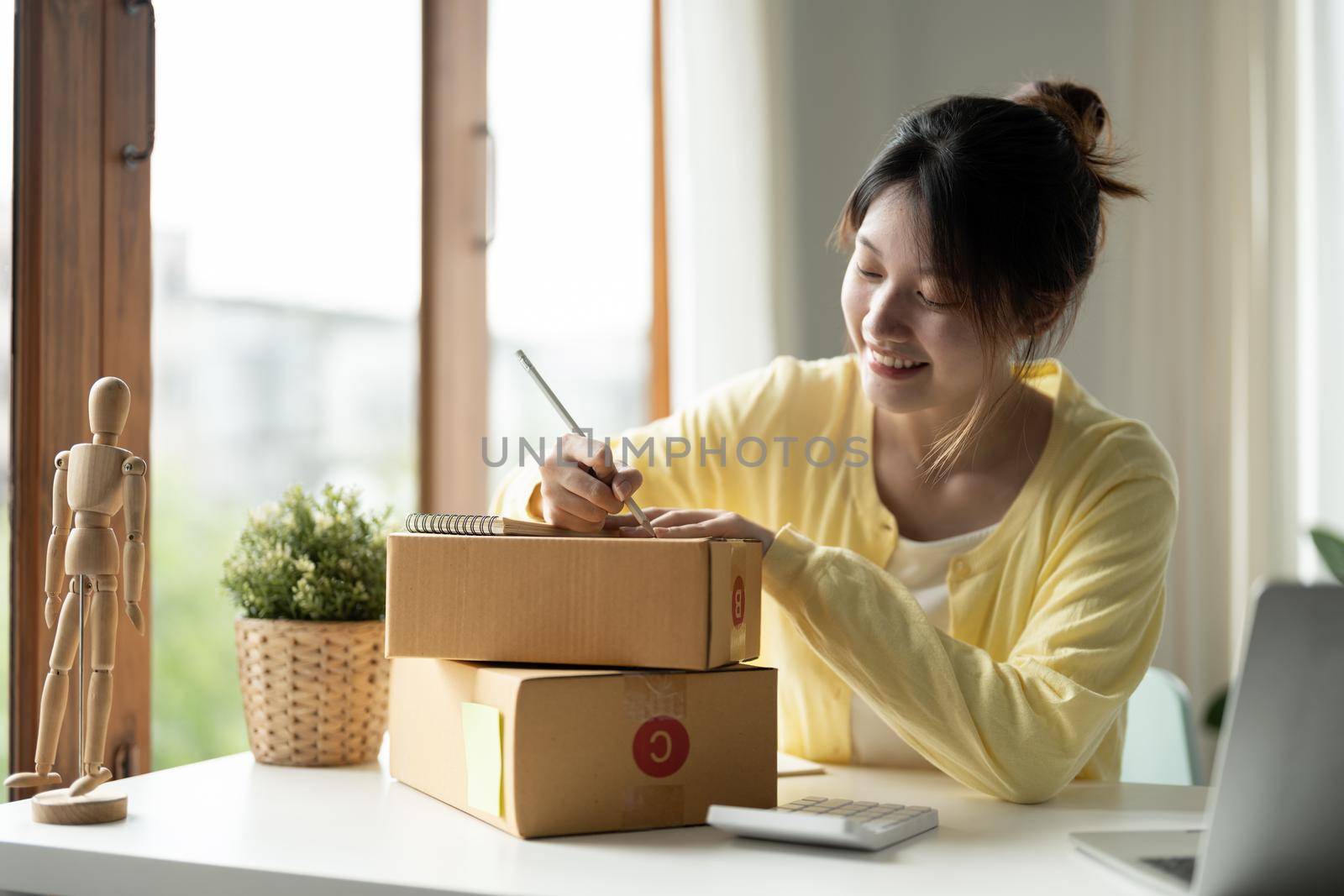 Young asian girl is freelancer Start up small business owner writing address on cardboard box at workplace,Shipping shopping online small business entrepreneur SME or freelance.