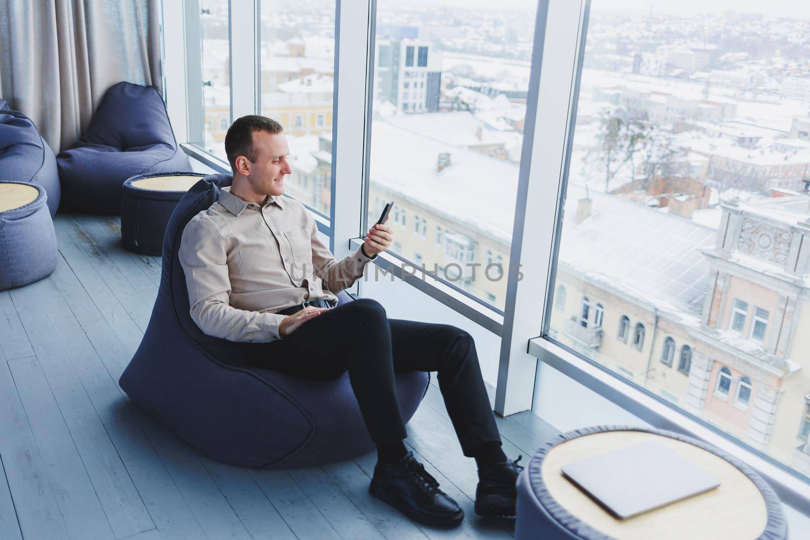 Successful male freelancer sitting in modern workspace and checking notifications on mobile phone in casual clothes. Remote work.