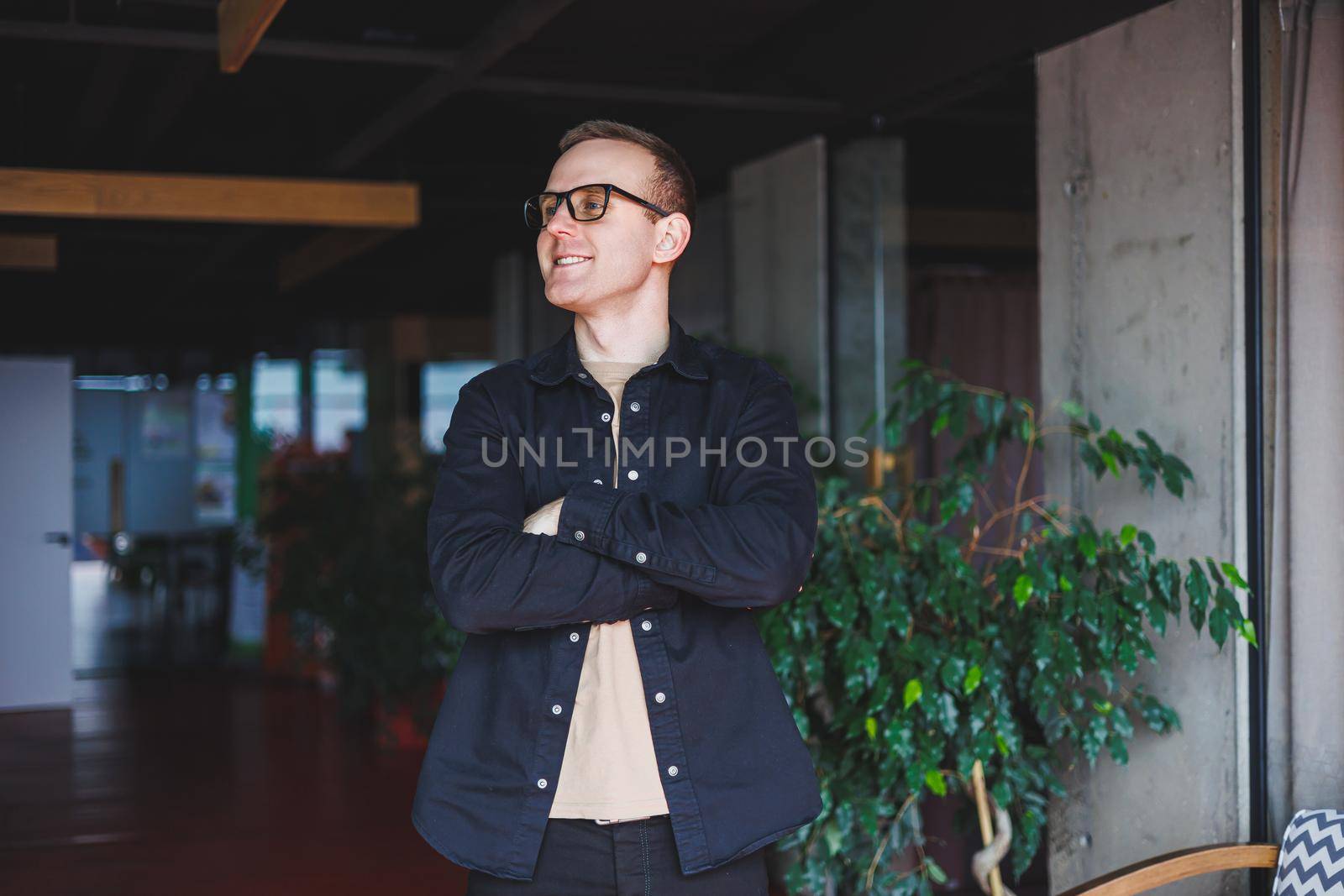 Half-length portrait of happy man in optical glasses holding modern mobile phone and smiling at camera, cheerful blogger with digital smartphone posing in coworking space by Dmitrytph