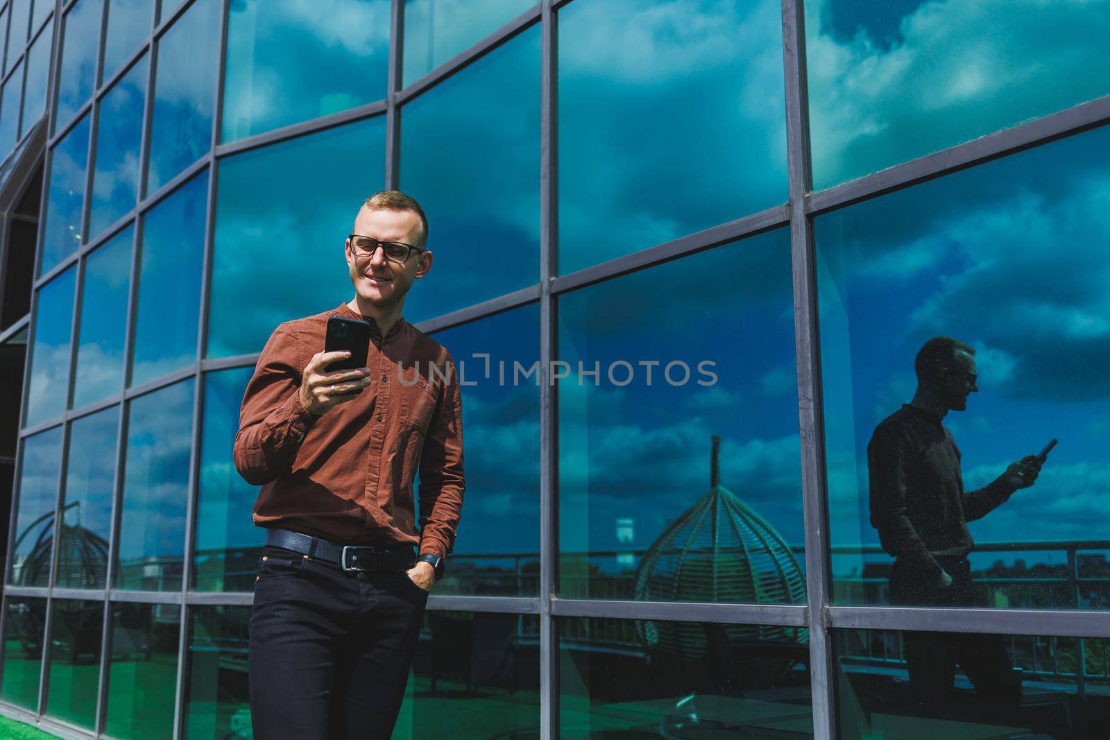 Happy man in classic glasses for vision correction with talking on terrace on mobile phone, smiling blogger browsing social media website