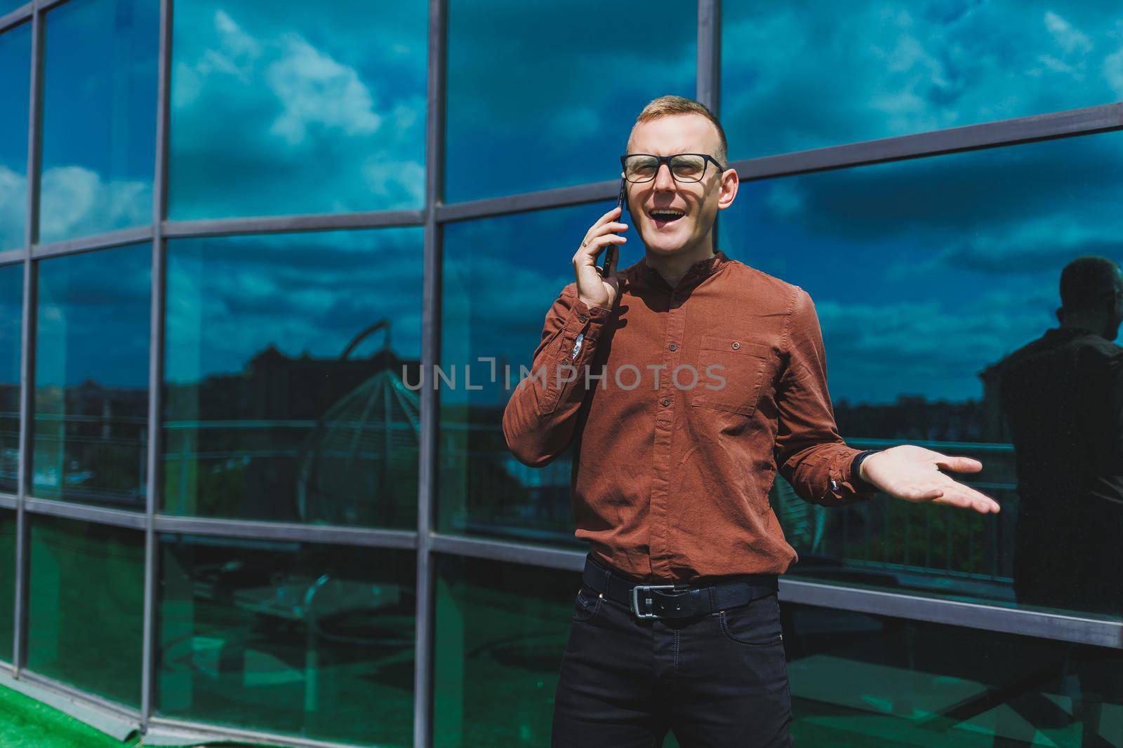 Happy man in classic glasses for vision correction with talking on terrace on mobile phone, smiling blogger browsing social media website